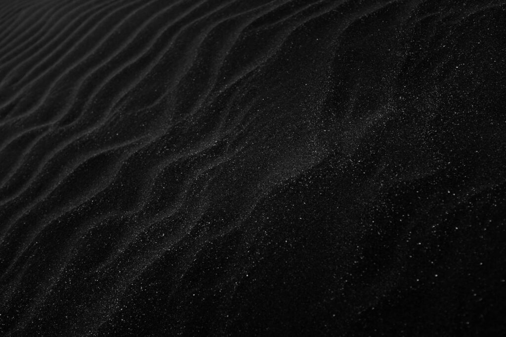 Textured black sand with ripples resembling dunes, creating a dark, abstract aesthetic.
