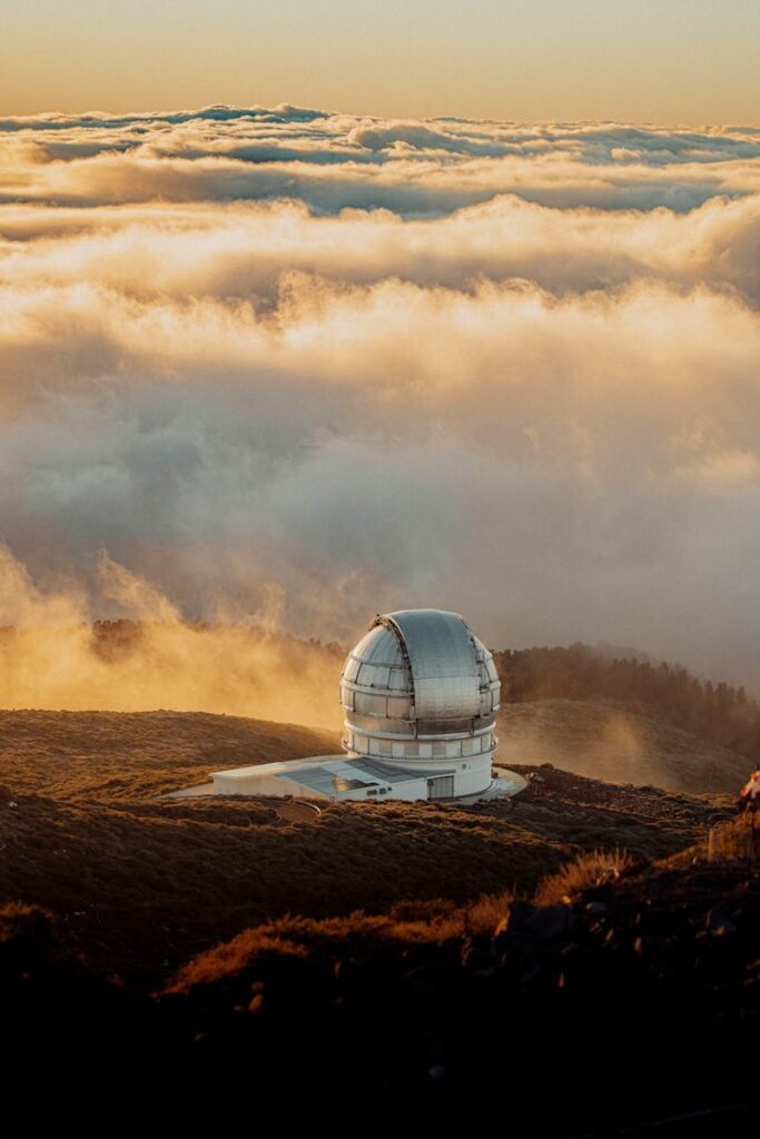 Telescope observatory overlooks clouds at sunset.