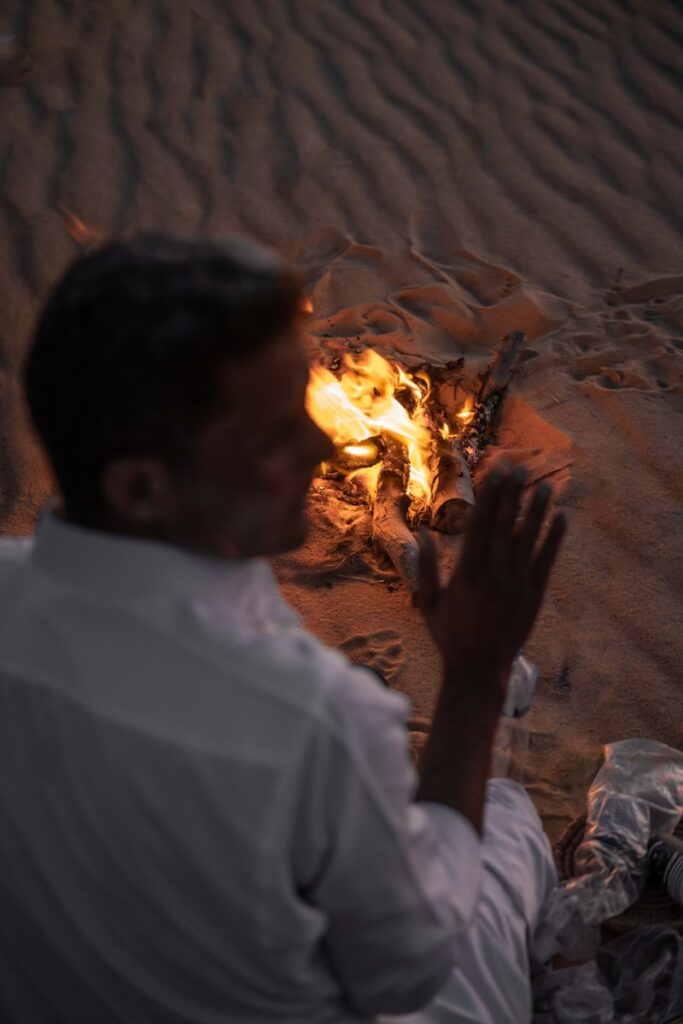 Man warms his hands by a desert campfire.