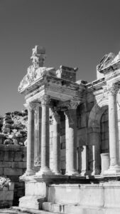 Black and white photo of ancient Roman ruins with detailed columns under a clear sky.