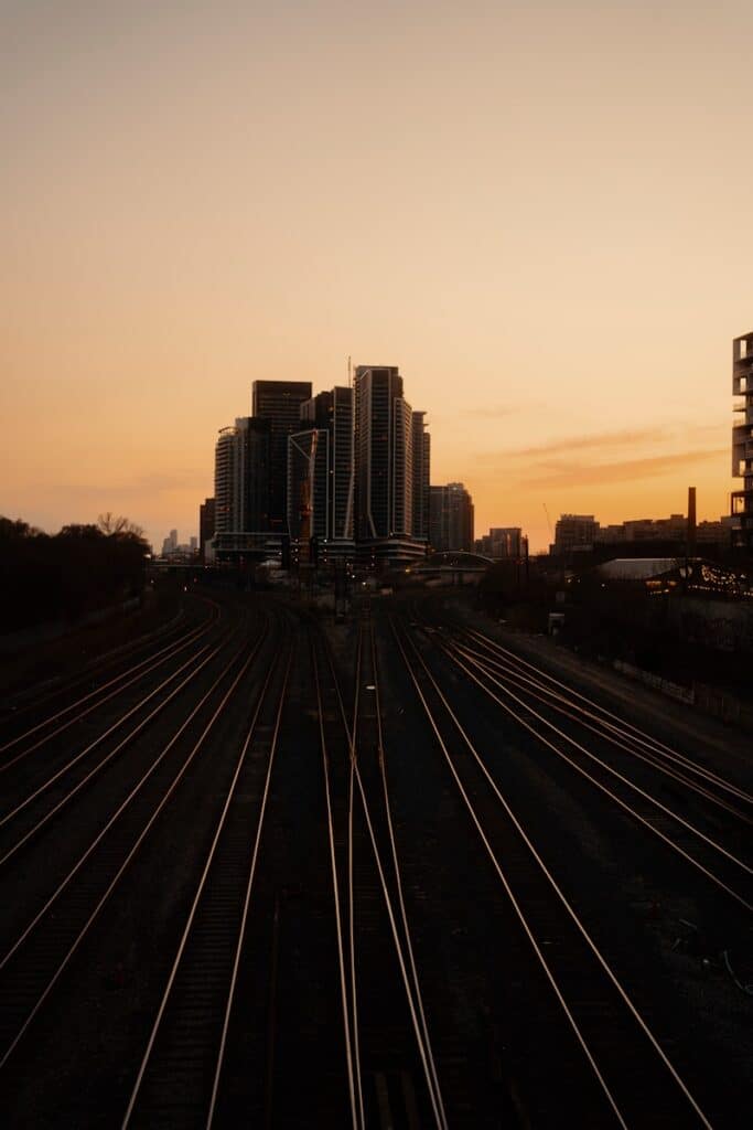 Railroad tracks lead to a city skyline at sunset.