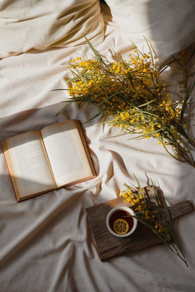 Book, flowers, and tea on a cozy bed.