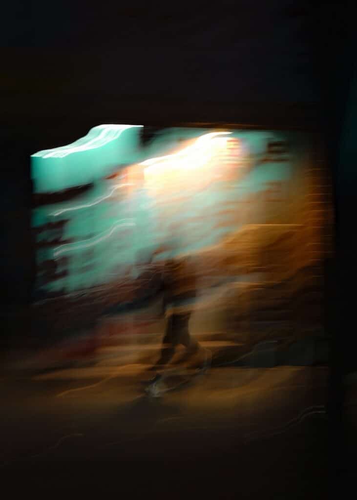 Blurred figure walking in front of a bright wall.