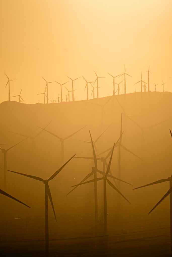 Wind turbines stand in a hazy, golden landscape.