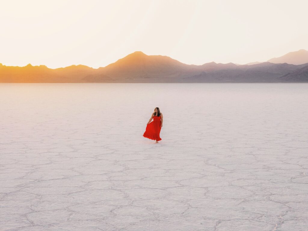 Woman in red dress walks across salt flats.