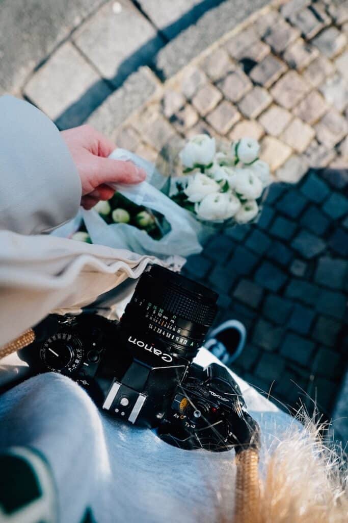 A camera sits with flowers in someone's hand.
