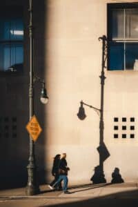 Two people walk by a building in sunlight.
