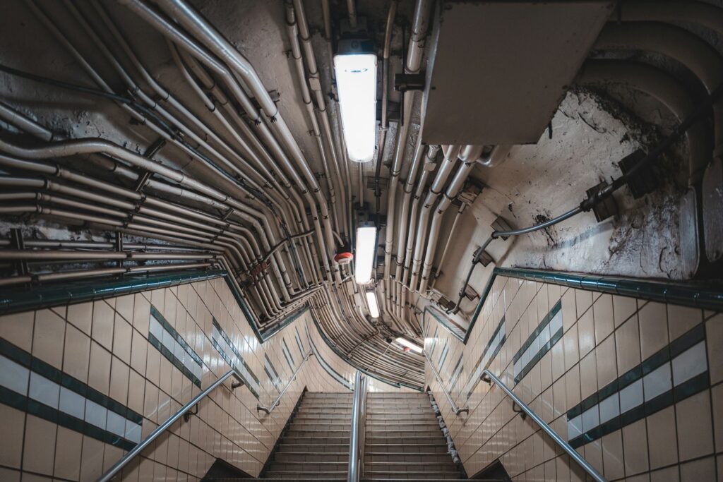 A stairway descends below numerous pipes and lighting.