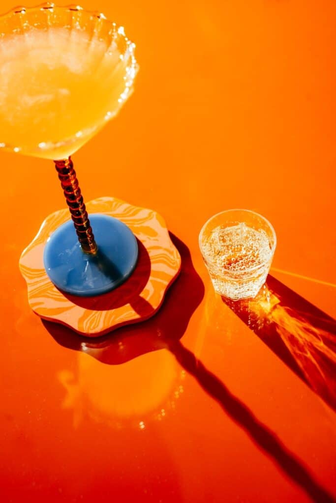 A cocktail and water on a bright orange surface.