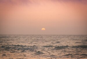 Sun setting over a vast, hazy ocean.